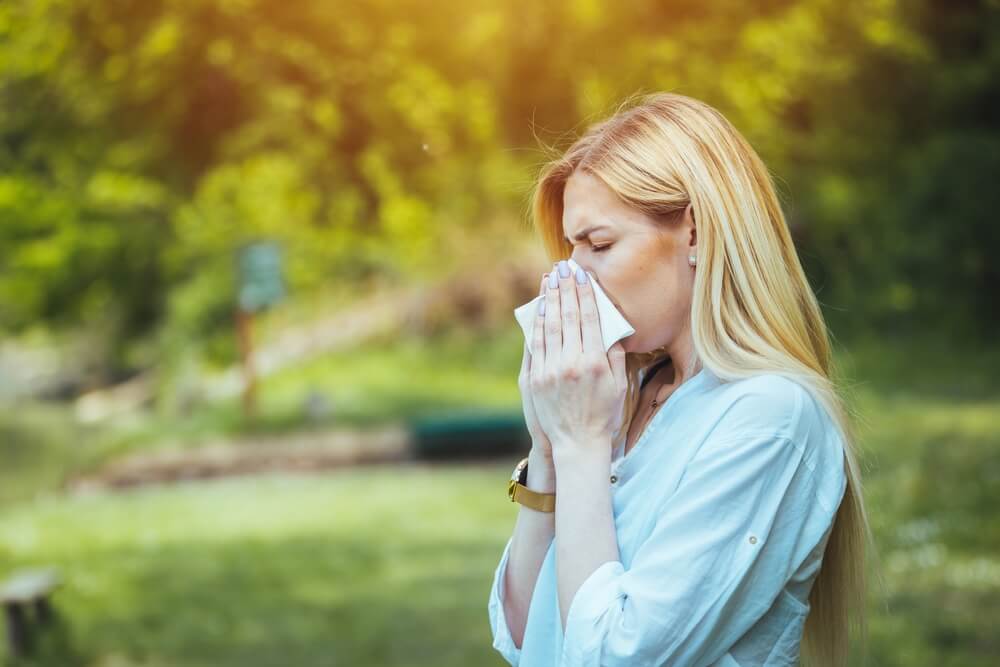 Mlada žena briše nos koji curi usled alergije izazvane polenom.